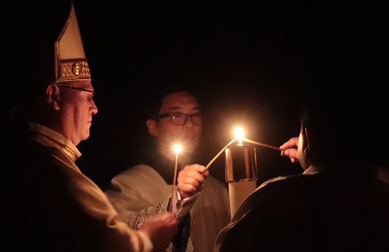Bishop Louis Tylka and Phillip Lee, director of the Office of Divine Worship, light their candles from the newly blessed Paschal Candle as the Easter Vigil begins at St. Mary's Cathedral in Peoria on April 8. Holding the Paschal Candle is Deacon Ignacio Cárdenas Morán, who would sing the Exsultet or Easter Proclamation. (The Catholic Post/Jennifer Willems)