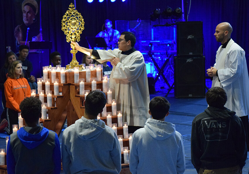 Phil Lee, director of the diocesan Office of Divine Worship, places a monstrance holding the Blessed Sacrament atop a tower of candles during a period of adoration at the Abide in Me youth retreat held Nov. 1-3 at Corpus Christi Catholic School in Bloomington. Father Eric Bolek, parochial vicar of St. Patrick Church of Merna, Bloomington, and St. Mary, Downs, is at right. (The Catholic Post/Tom Dermody)